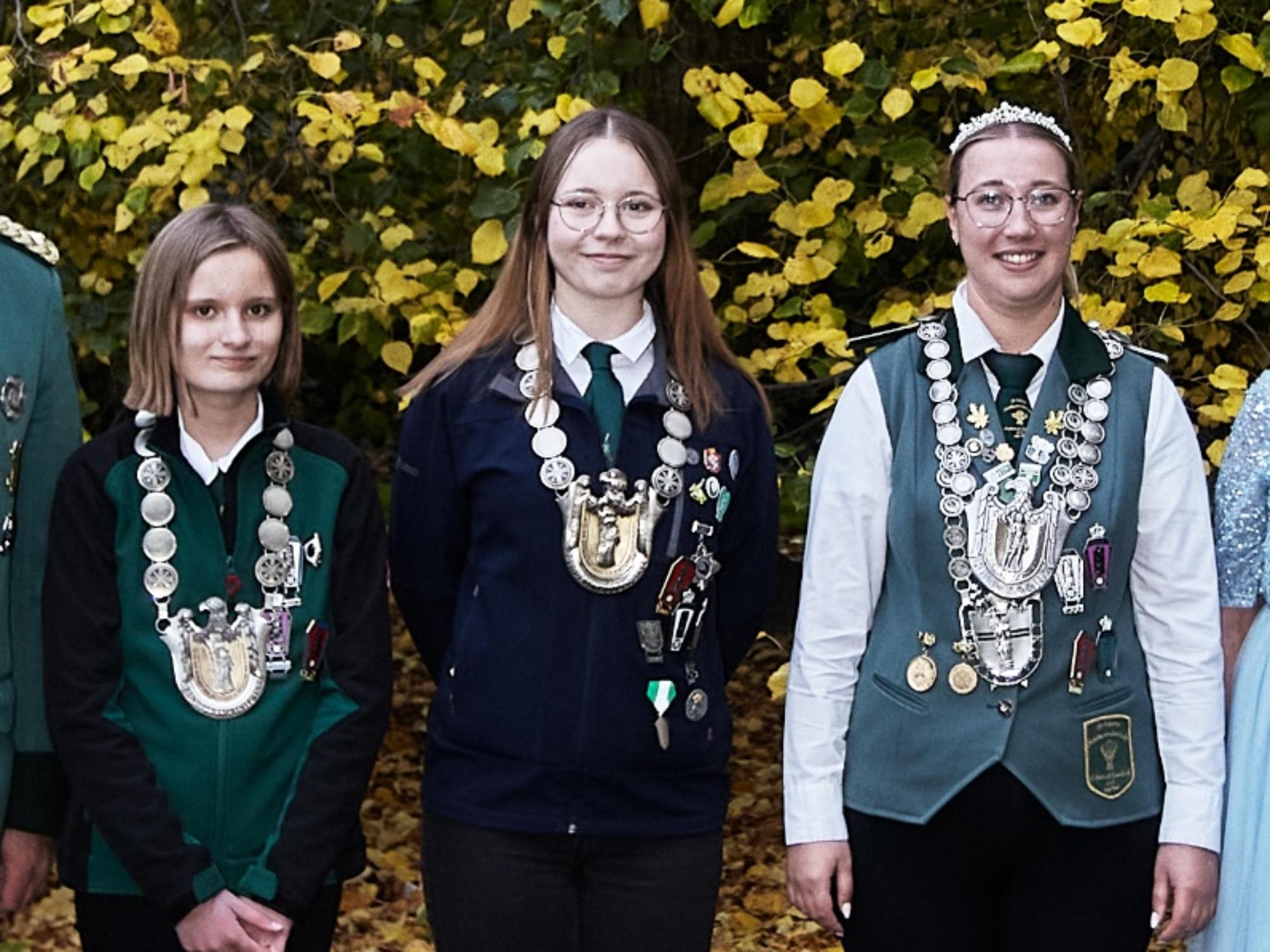 Zu sehen sind die drei neuen Bundesprinzessinen mit ihren Ketten, fotografiert vor einem Gebüsch